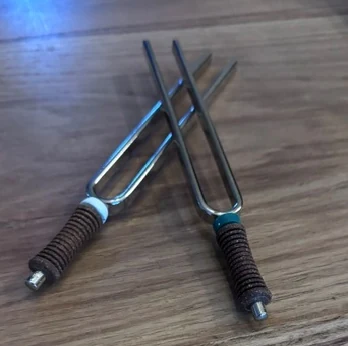 Zwei Stimmgabeln mit umwickelten Stielen auf einem Holztisch